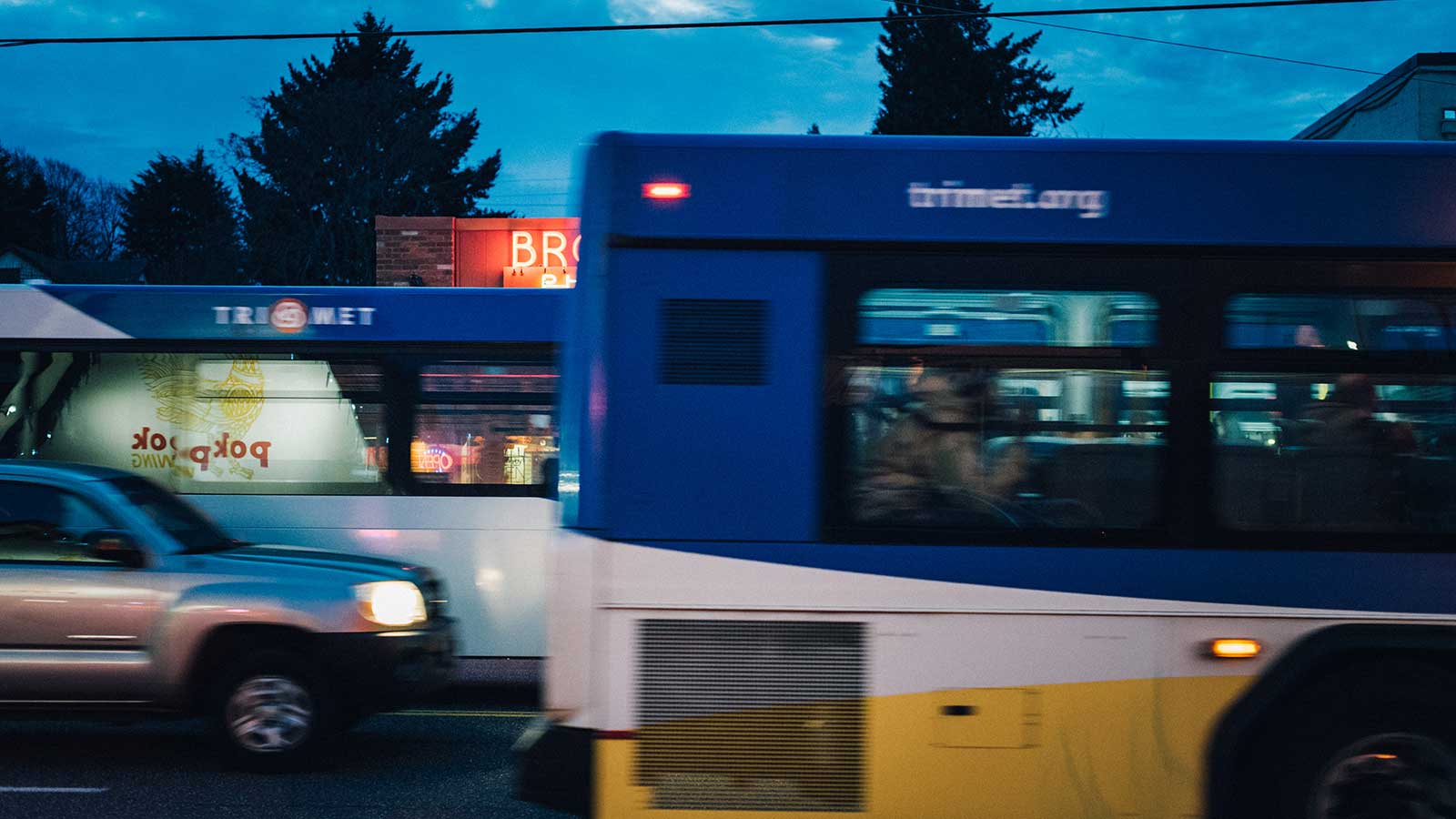 Buses in traffic at dusk with signs reflecting in the windows