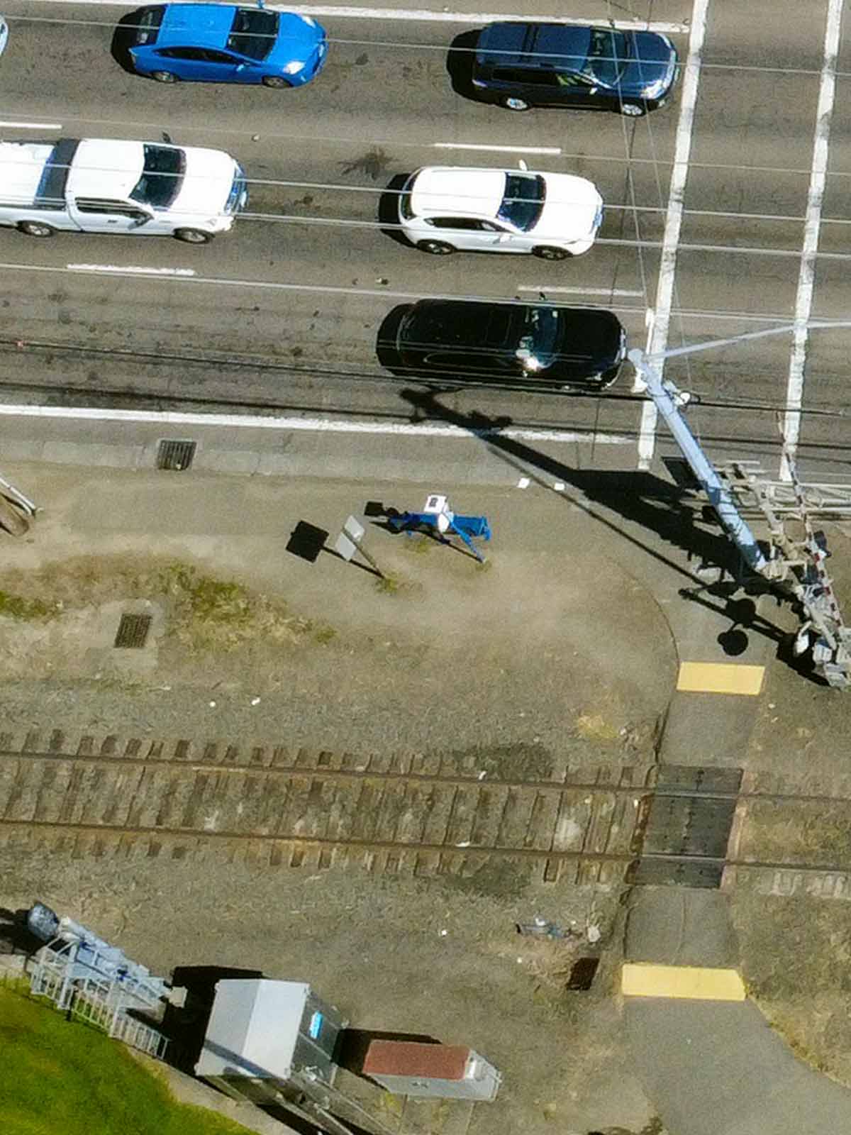 Photo showing a person waiting at a bus stop. The bus stop consists of a broken slab of asphalt perched atop weeds, gravel and trash.