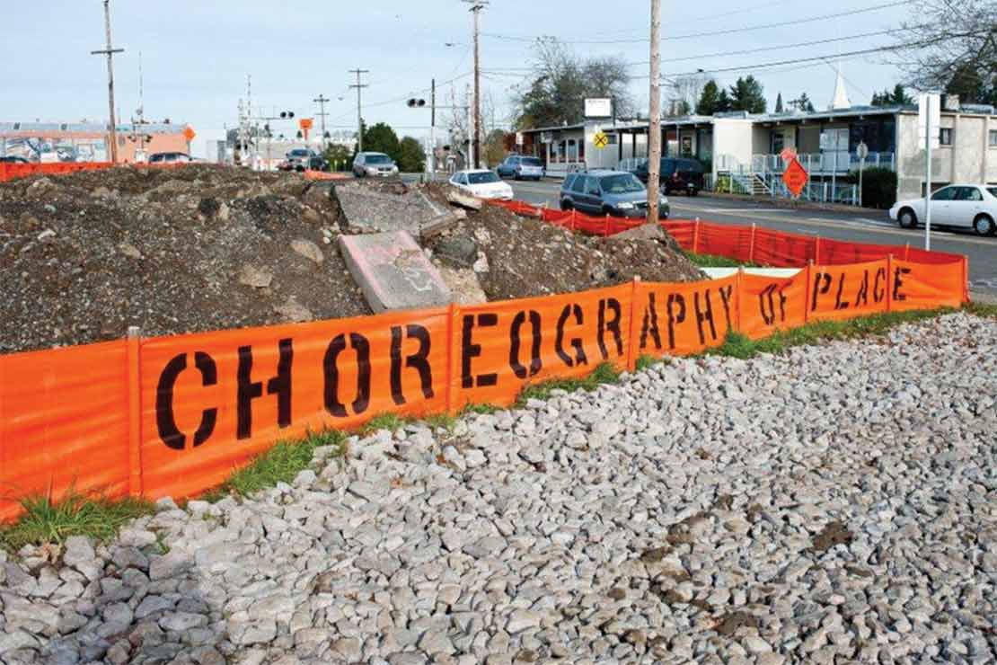 Polypropylene fencing with the phrase 'Choreography of Place' surrounds a pile of broken concrete